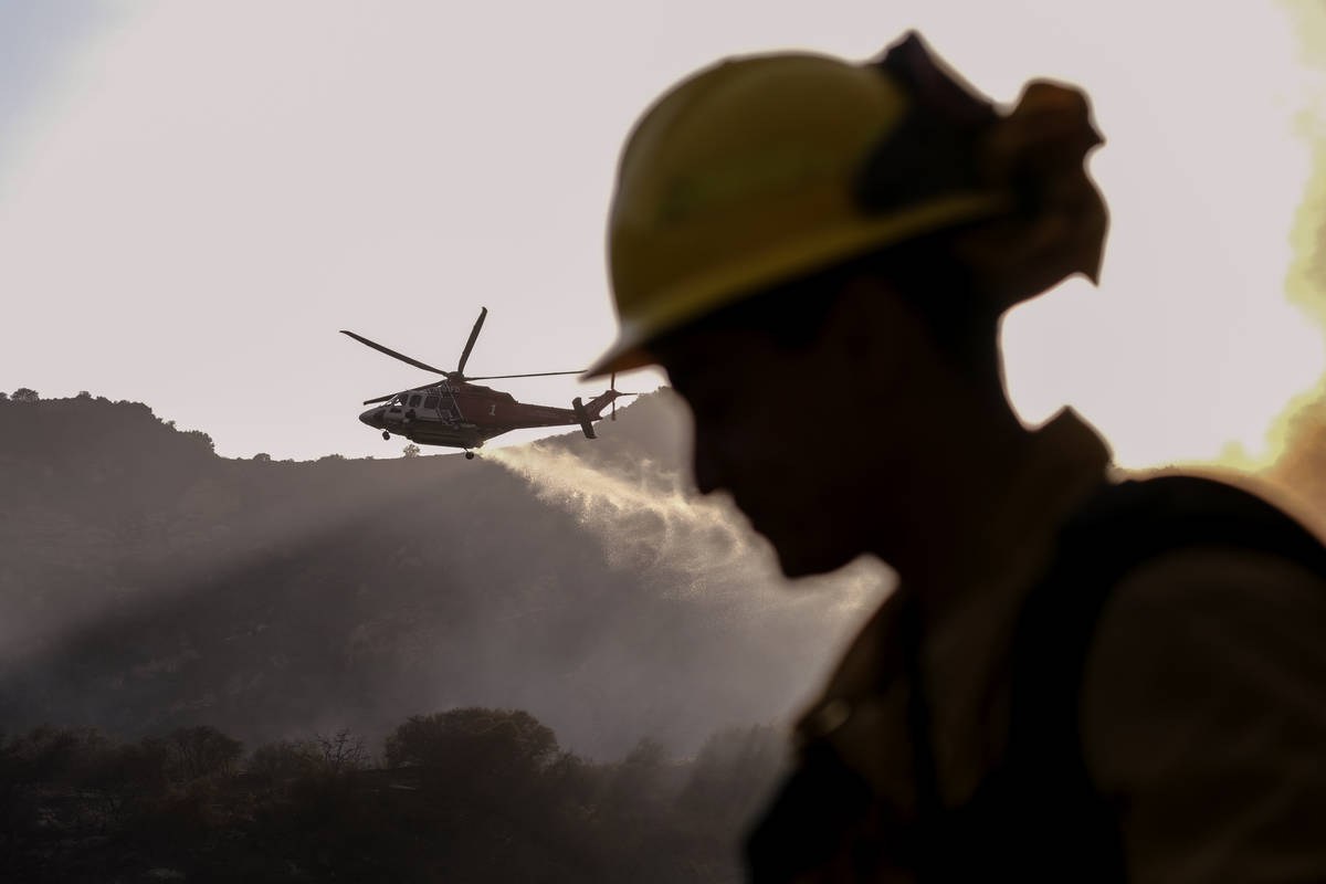 A firefighter keeps watch as a firefighting helicopter drops water on a brush fire scorching at ...