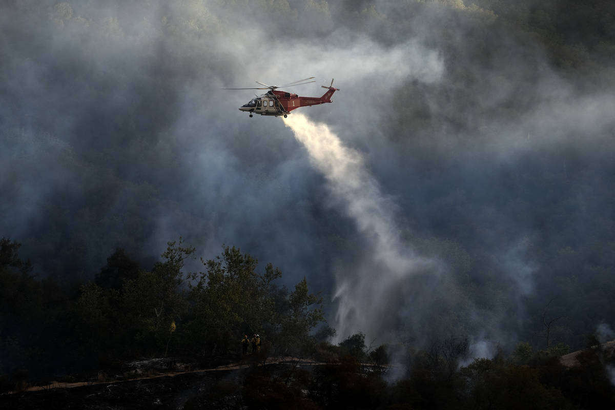 A firefighting helicopter drops water onto a brush fire scorching at least 100 acres in the Pac ...
