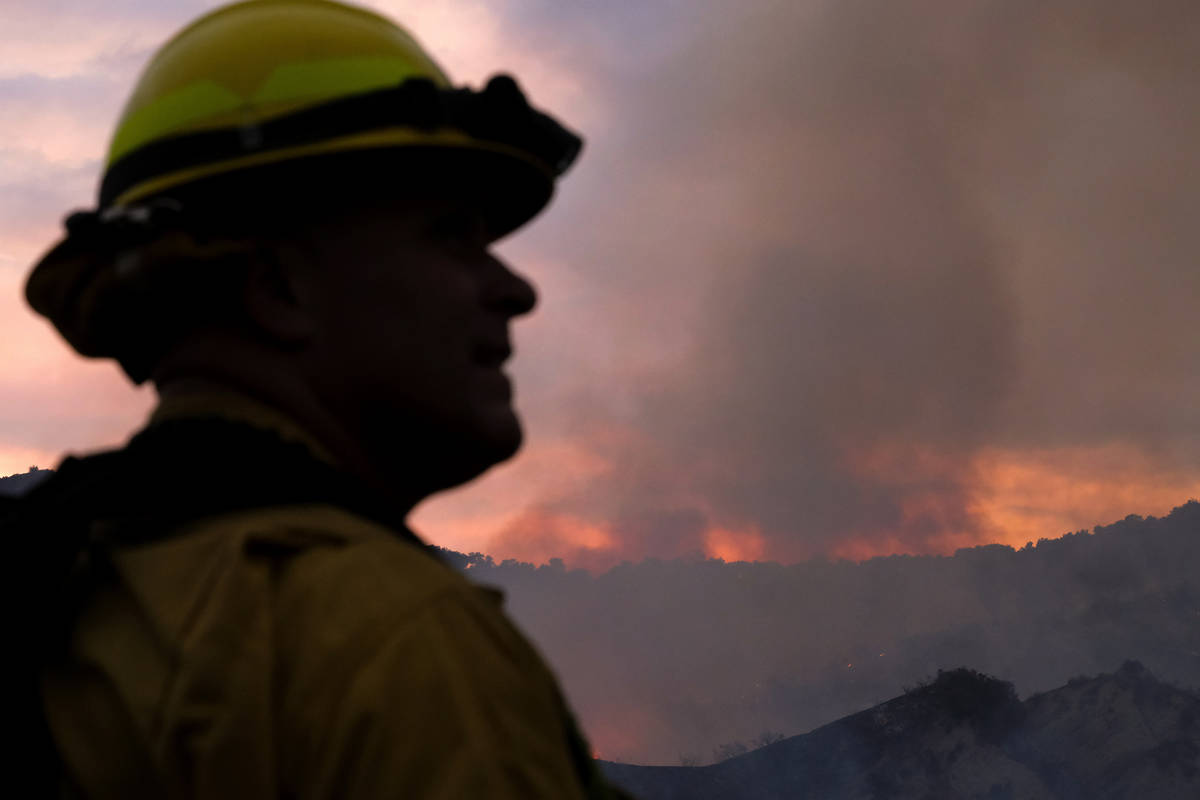 A firefighter keeps watch as smoke rises from a brush fire scorching at least 100 acres in the ...