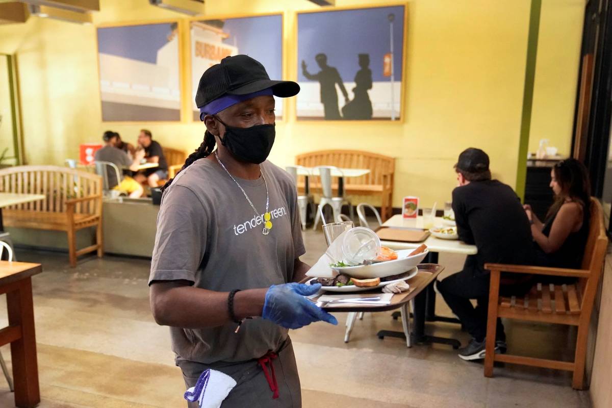 A worker in a face mask clears tables inside a covered patio amid the COVID-19 pandemic Tuesday ...