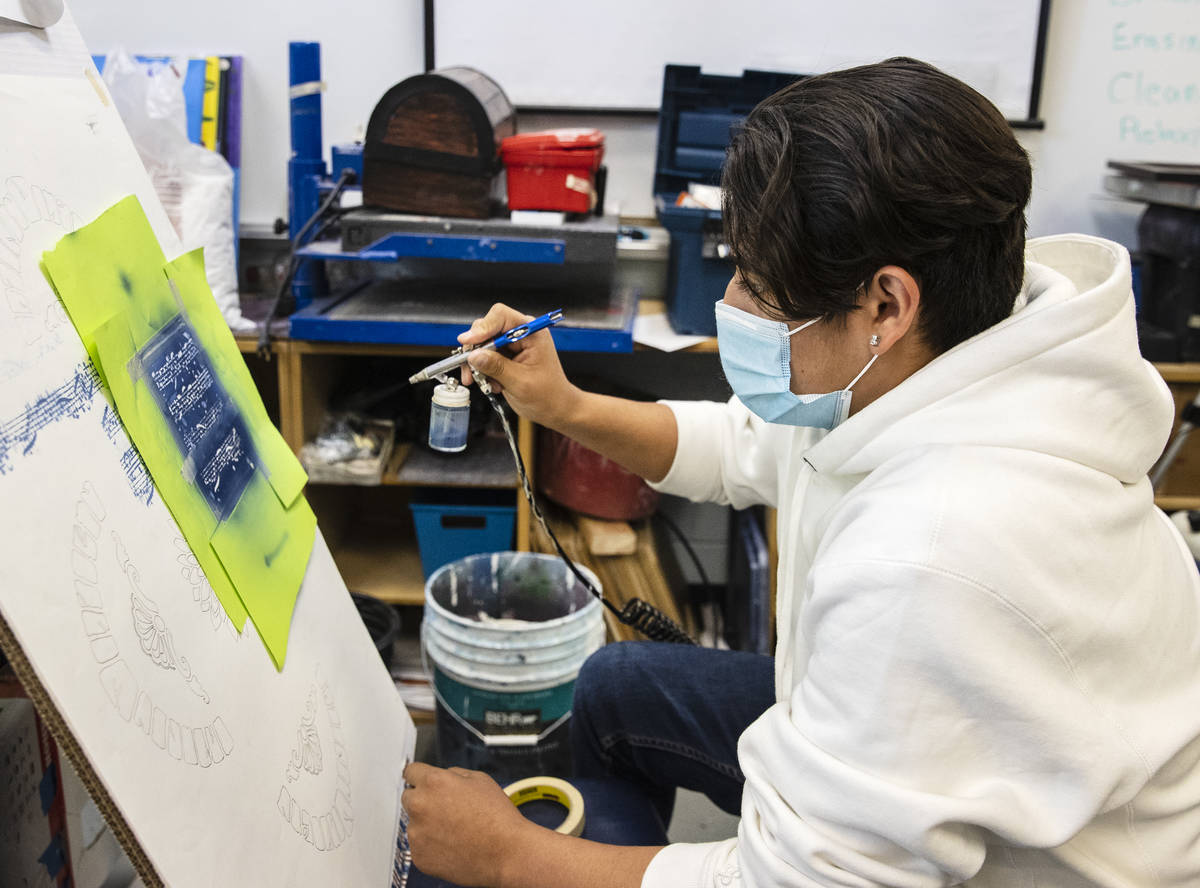 Global Community High School senior Edgar Avalos sprays paint over music notes during art class ...