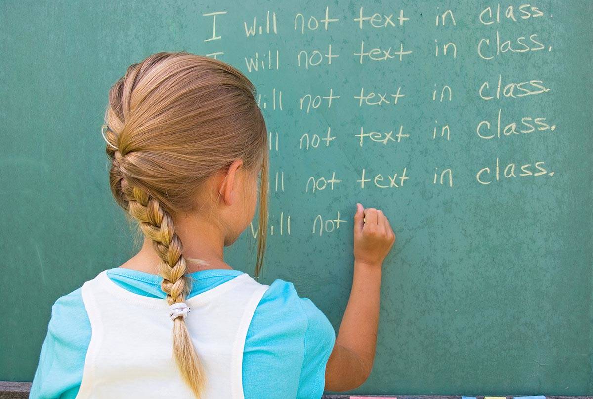 Little girl writing lines on a green chalkboard in school.