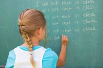 Little girl writing lines on a green chalkboard in school.