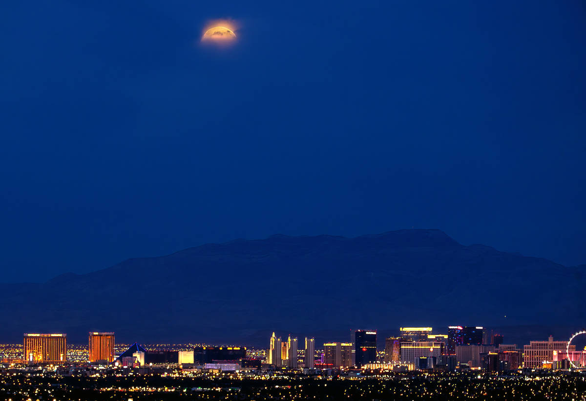A Super Flower Blood Moon and lunar eclipse peeks out from the clouds while setting beyond the ...
