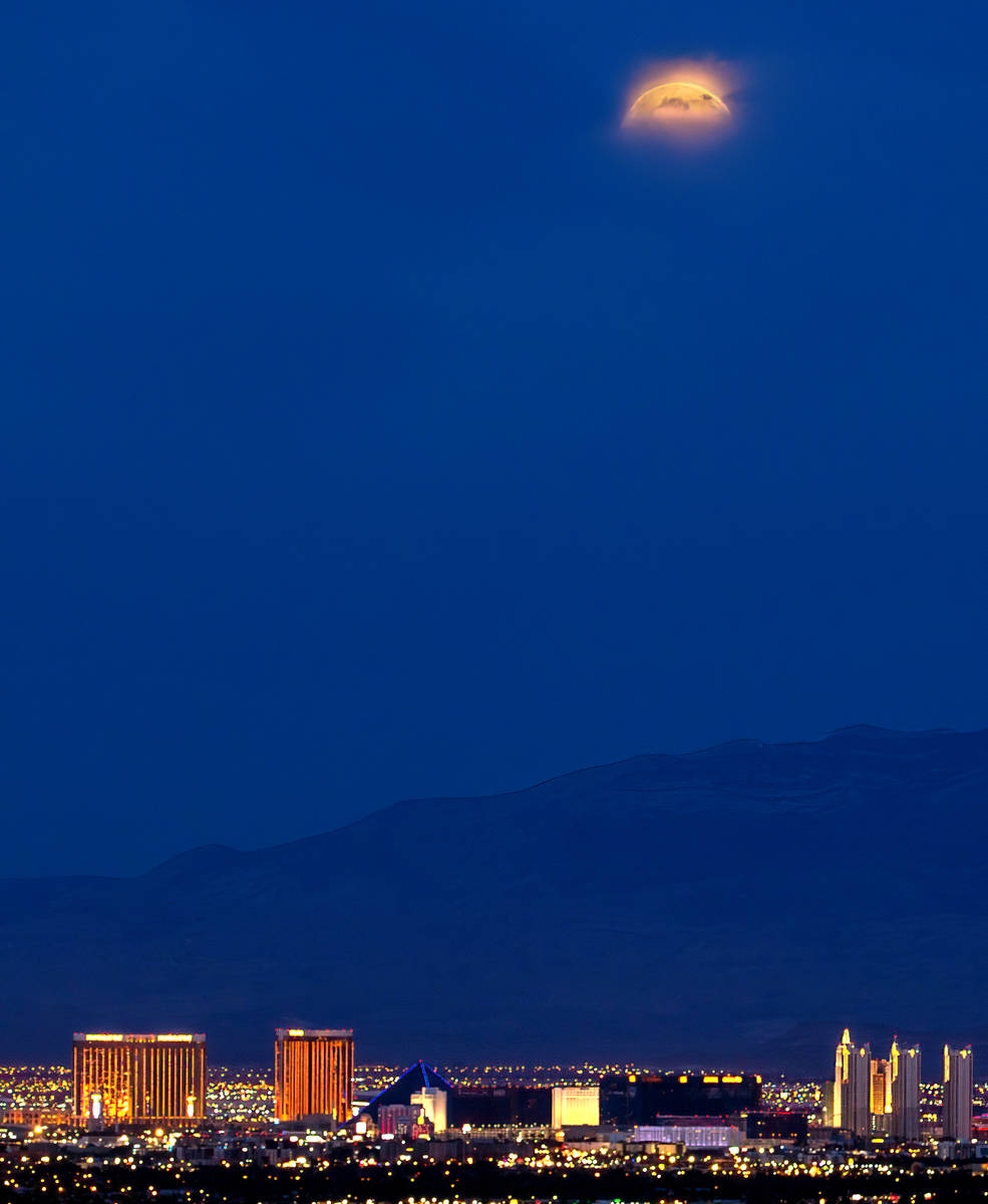 A Super Flower Blood Moon and lunar eclipse peeks out from the clouds while setting beyond the ...