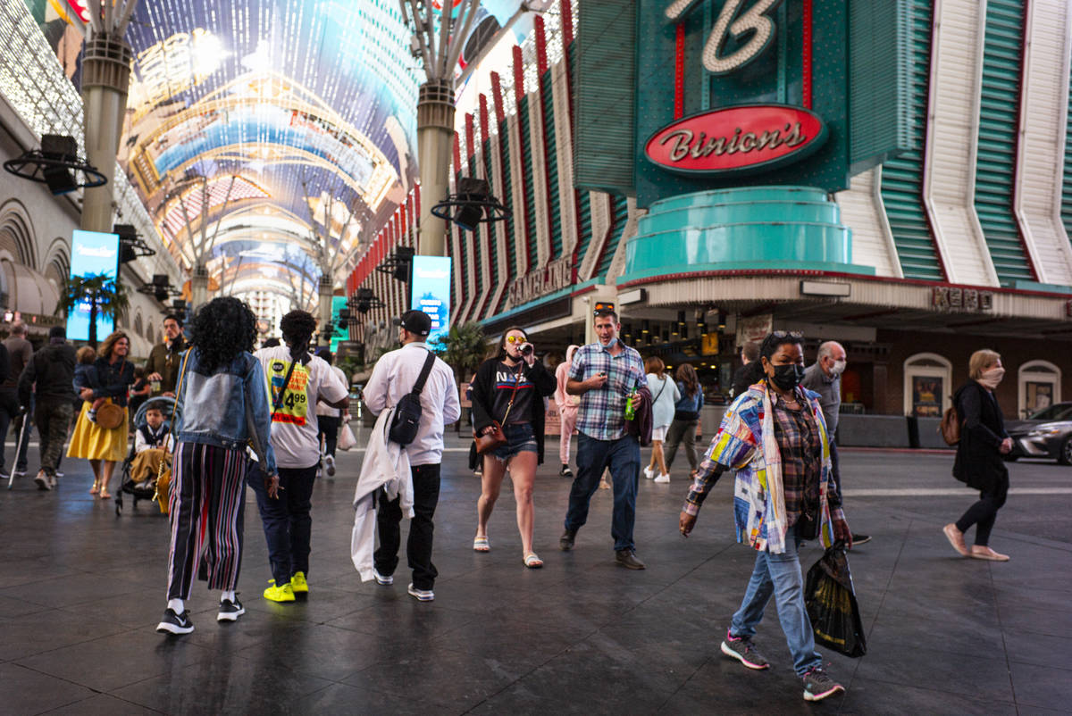 People, some wearing masks and others not, walk around the Fremont Street Experience in downtow ...