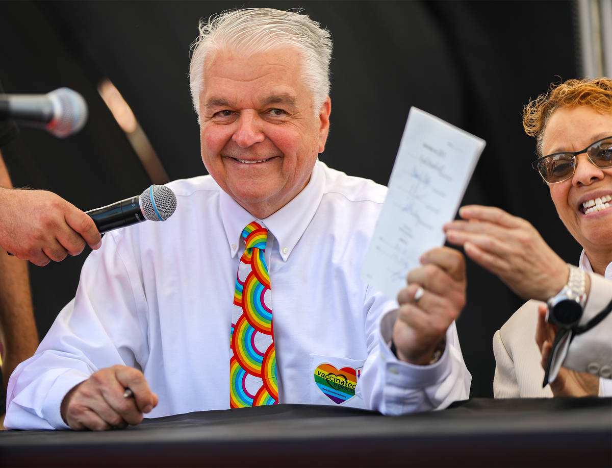 Gov. Steve Sisolak, left, holds up one the bills he signed that helps the LGBTQ community along ...