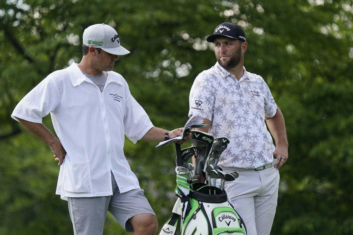 Jon Rahm talks with his caddie as he waits to hit on the 14th tee during the third round of the ...