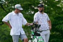 Jon Rahm talks with his caddie as he waits to hit on the 14th tee during the third round of the ...