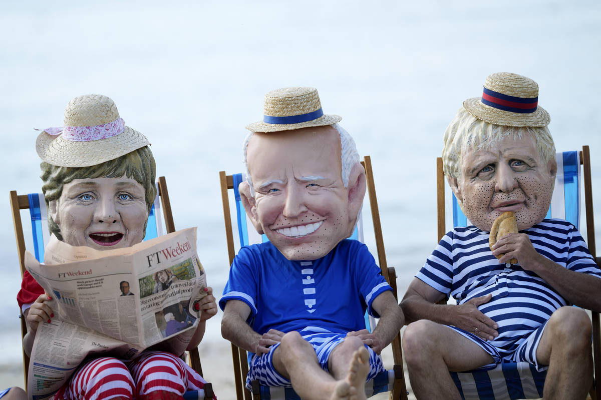 Climate activists from Oxfam, wearing giant heads depicting the leaders of the G7, sit on beach ...
