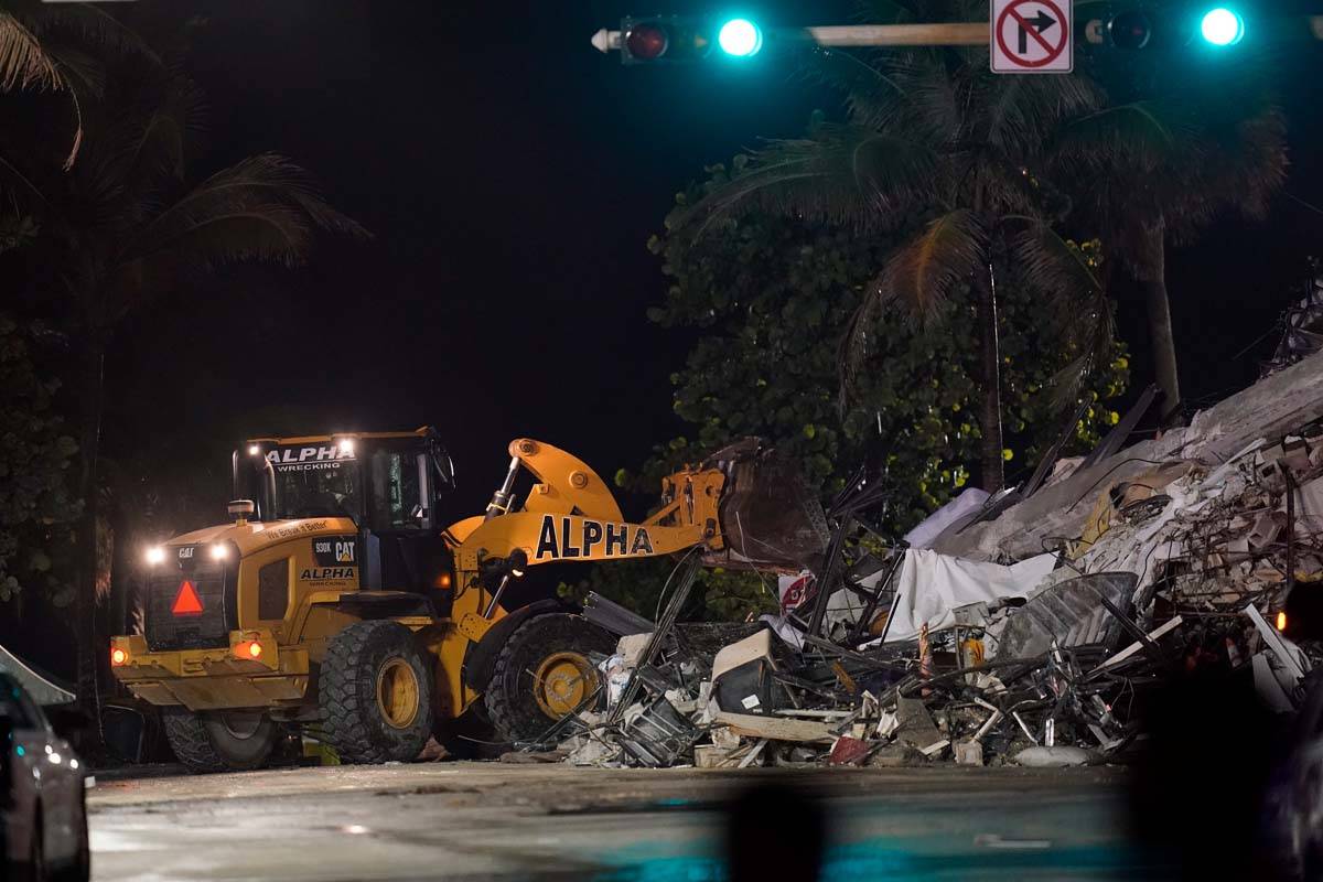 A front end loader shifts rubble mixed with furniture and household items, as rescue efforts co ...