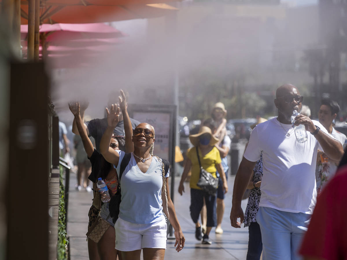 Visitors cool off in the misters outside the Paris Las Vegas as the temperature rises on Saturd ...