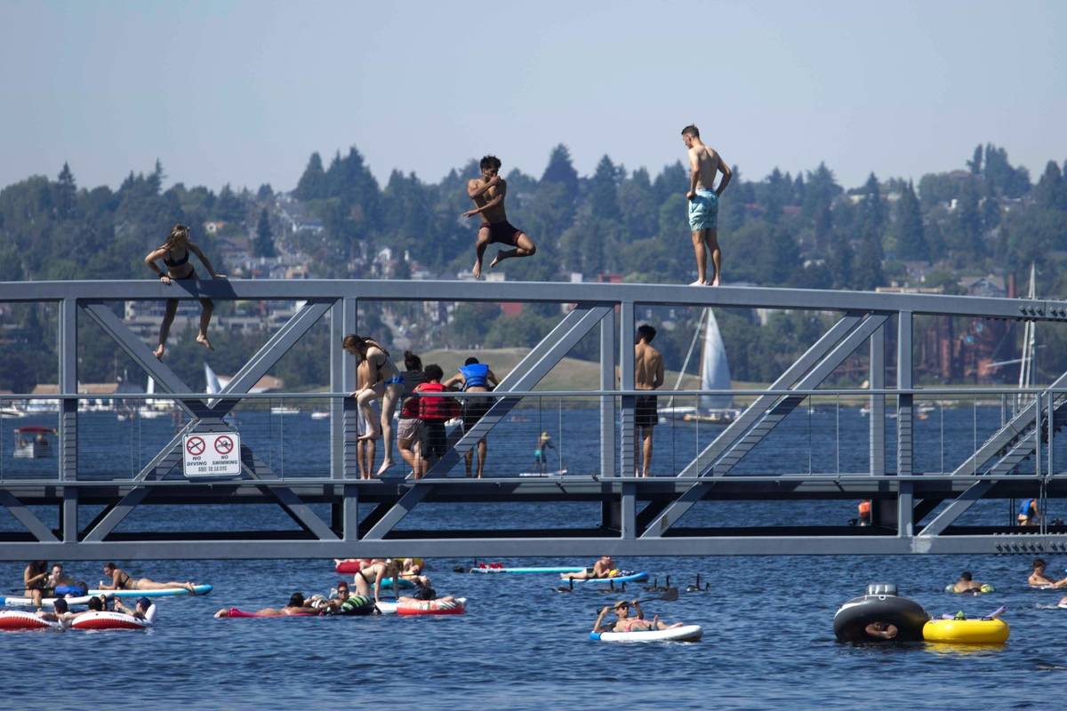 Two people jump from a pedestrian bridge at Lake Union Park into the water during a heat wave h ...