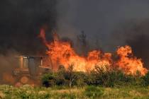 A bulldozer operator works on a fire line as vegetation burns nearby at the Lava Fire on Monday ...