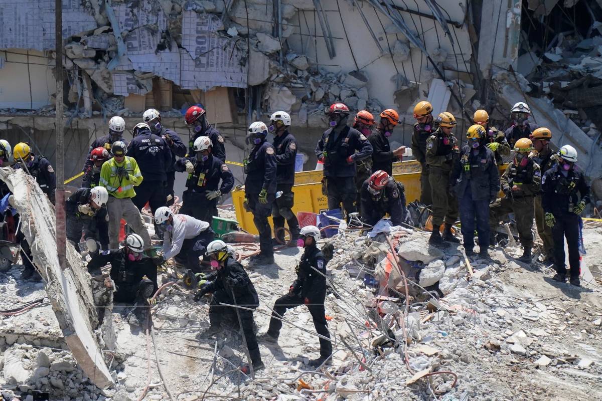 Search and rescue personnel help a colleague, as they work atop the rubble at the Champlain Tow ...