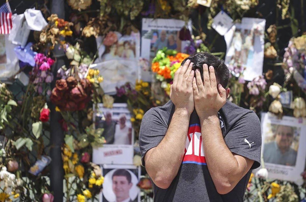 A man breaks down and shields his face with his hands as Surfside residents and passers-by stop ...