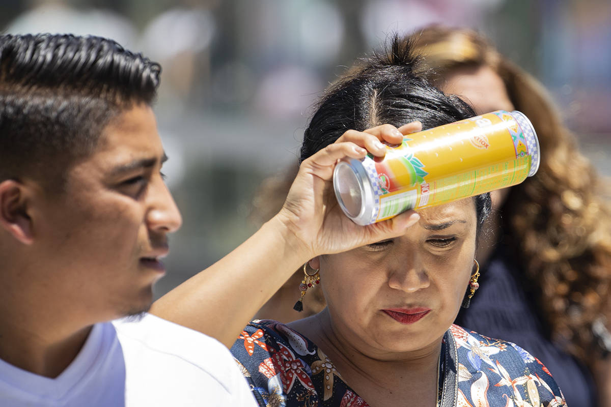 A pedestrian places a can of soda on her forehead to cool herself as she walks along Las Vegas ...