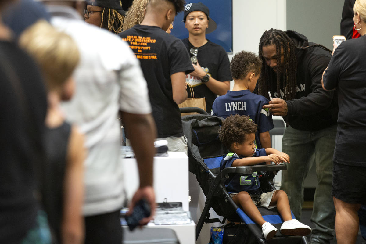 NFL running back Marshawn Lynch signs a jersey for Romeo Havard, 5, among fans and customers at ...