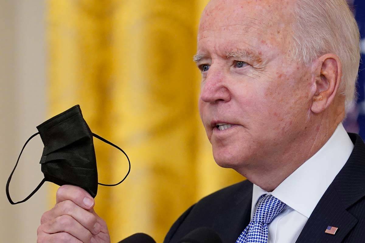 President Joe Biden holds up his face mask as he speaks about vaccine requirements for federal ...