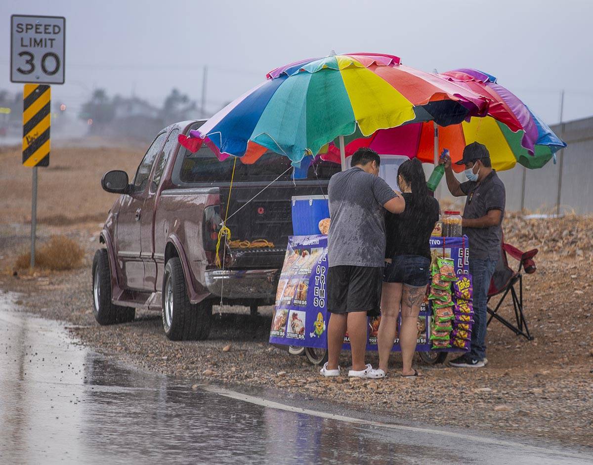 People stop for a bite to eat under some umbrellas of a cart vendor along West Twain Avenue as ...