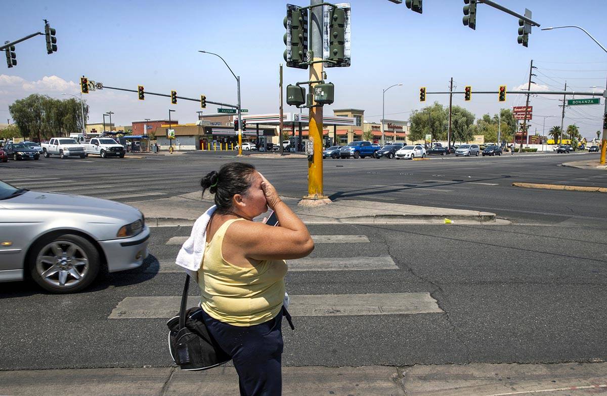 A woman wipes sweat from her face while walking at the intersection of North Eastern Avenue and ...