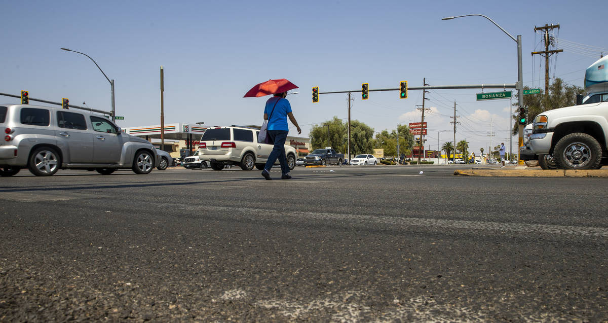 A woman with an umbrella for shade walks at the intersection of North Eastern Avenue and East B ...
