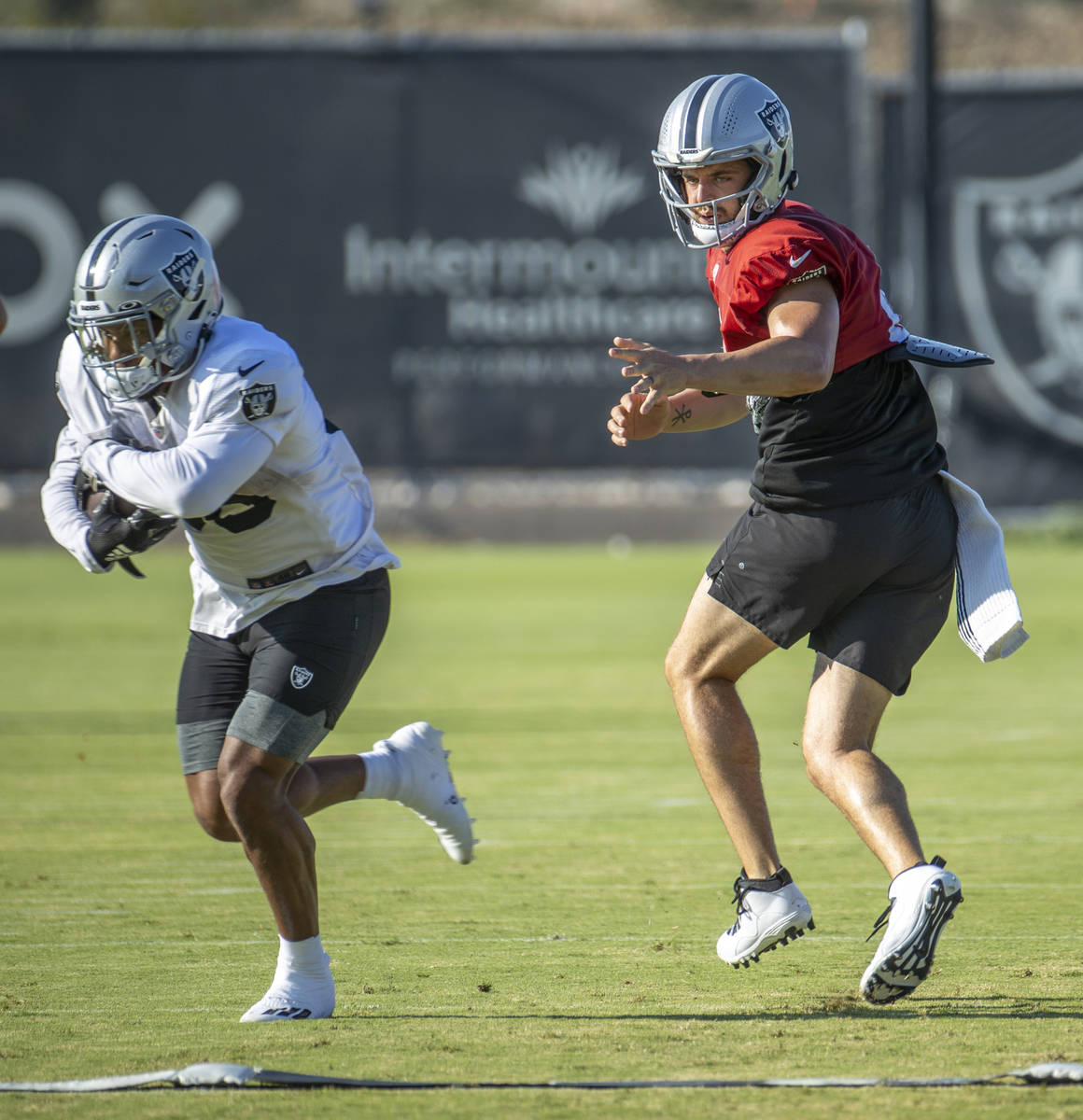 Raiders quarterback Derek Carr (4, right) looks on as he hands off the ball during practice at ...
