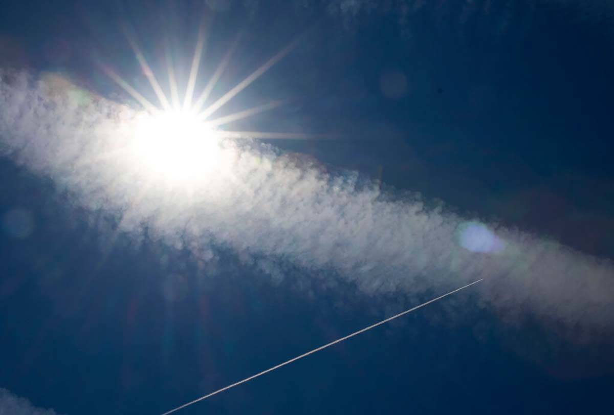 The shining sun and multiple jet streams are seen as an aircraft flies over Boulder Beach at La ...