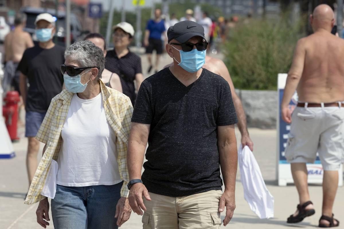 People wear protective masks while walking along the shoreline at Revere Beach, Saturday, Aug. ...
