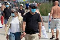 People wear protective masks while walking along the shoreline at Revere Beach, Saturday, Aug. ...