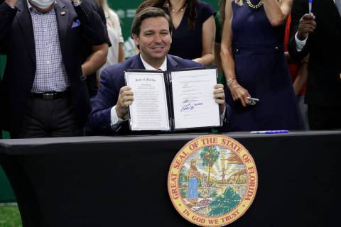 Florida Gov. Ron DeSantis holds up a just signed bill which would allow college athletes in the ...