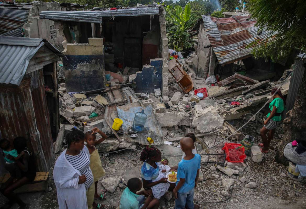 A family eats breakfast in front of homes destroyed by a 7.2 magnitude earthquake in Les Cayes, ...