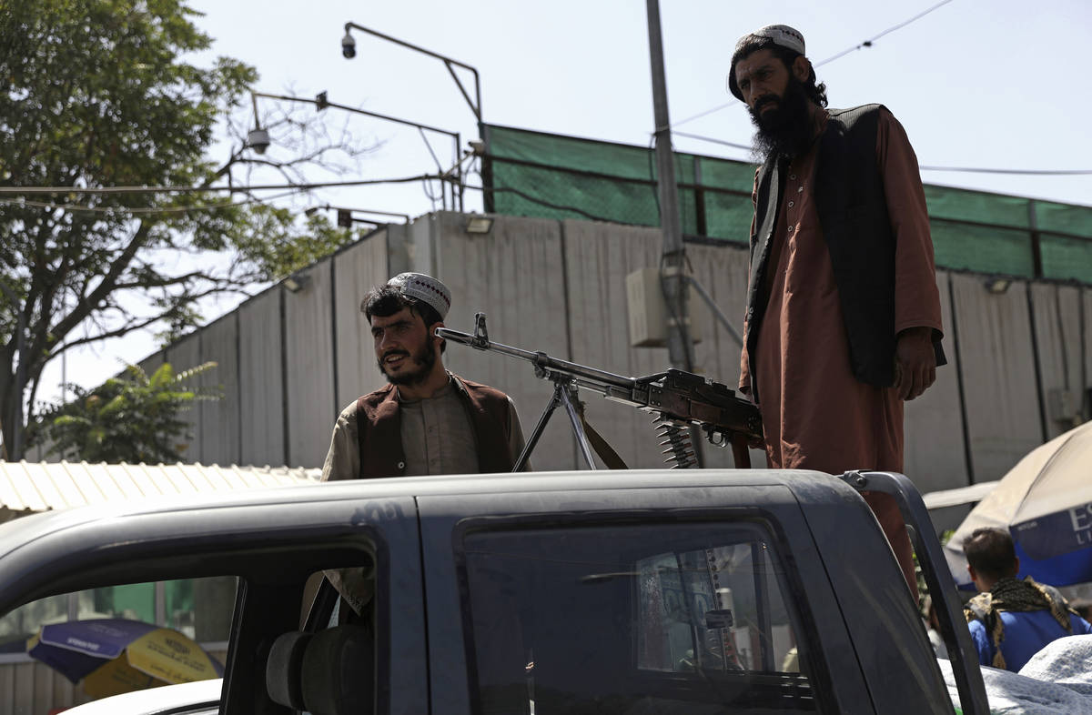 Taliban fighters stand guard on the back of vehicle with a machine gun in front of main gate le ...