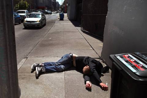 A man lies on the sidewalk beside a recyclable trash bin in San Francisco in April 2018. (AP P ...