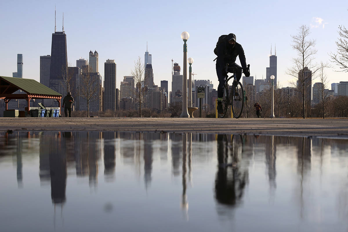 The Chicago skyline is reflected in the water of the thawed snow as a cyclist passes by at Nort ...