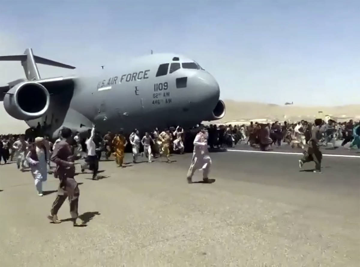 Hundreds of people run alongside a U.S. Air Force C-17 transport plane as it moves down a runwa ...