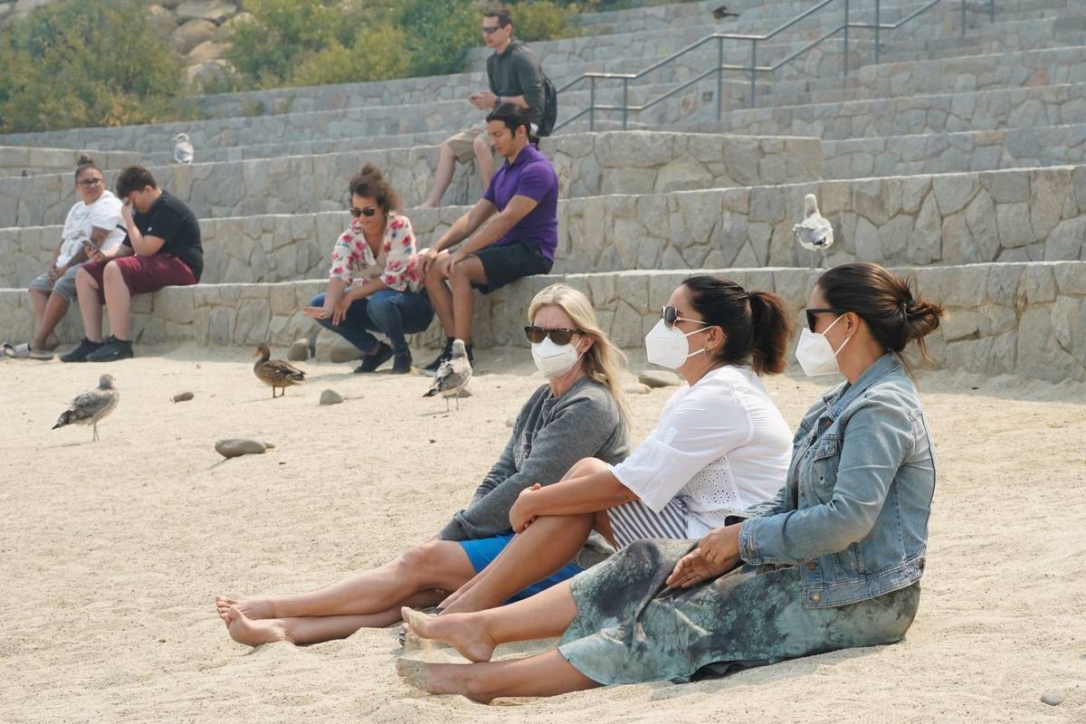 Amanda Abel, left, Kristy Weaver, center, and Kerry Murphy wear face masks as they sit along th ...