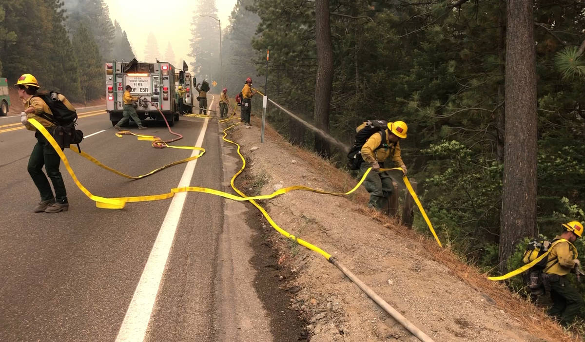 Fire crews carry a hose down a hill as the Caldor Fire burns on both sides of Highway 50 about ...
