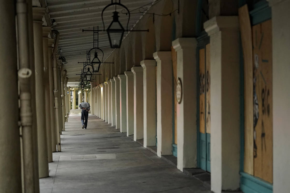 A man walks along businesses with protective boarding in the French Quarter as the early effect ...