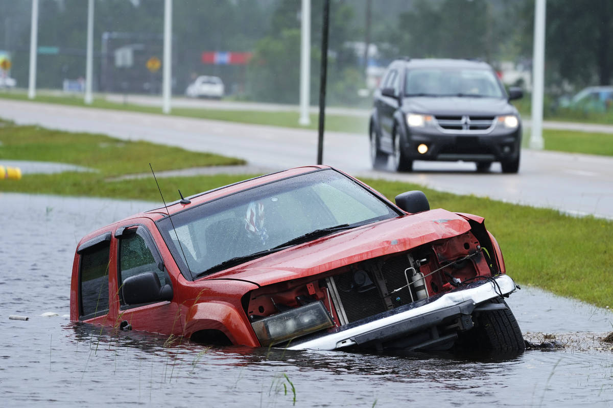 An abandoned vehicle is half submerged in a ditch next to a near flooded highway as the outer b ...
