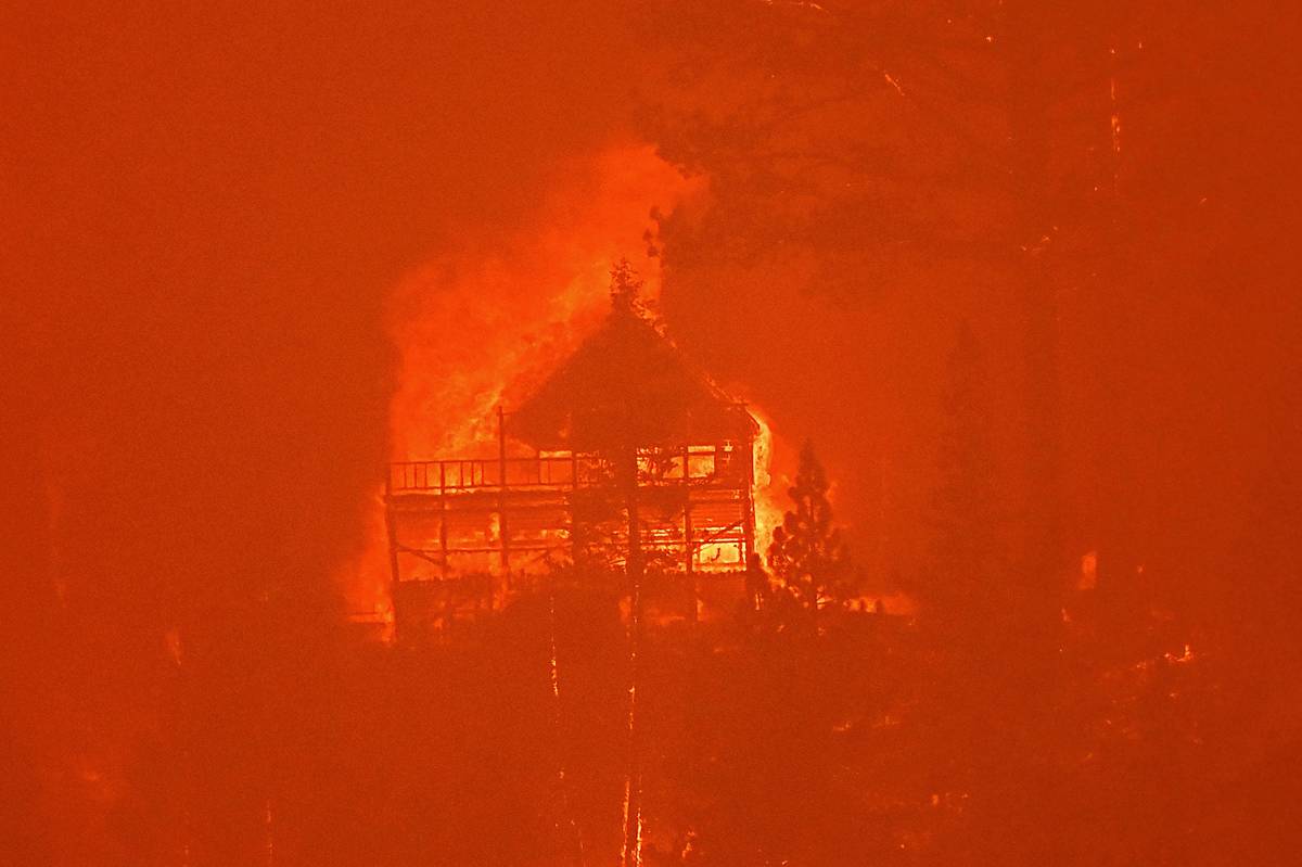 Seen from South Lake Tahoe, Calif., flames from the Caldor Fire consume a home on Monday, Aug. ...