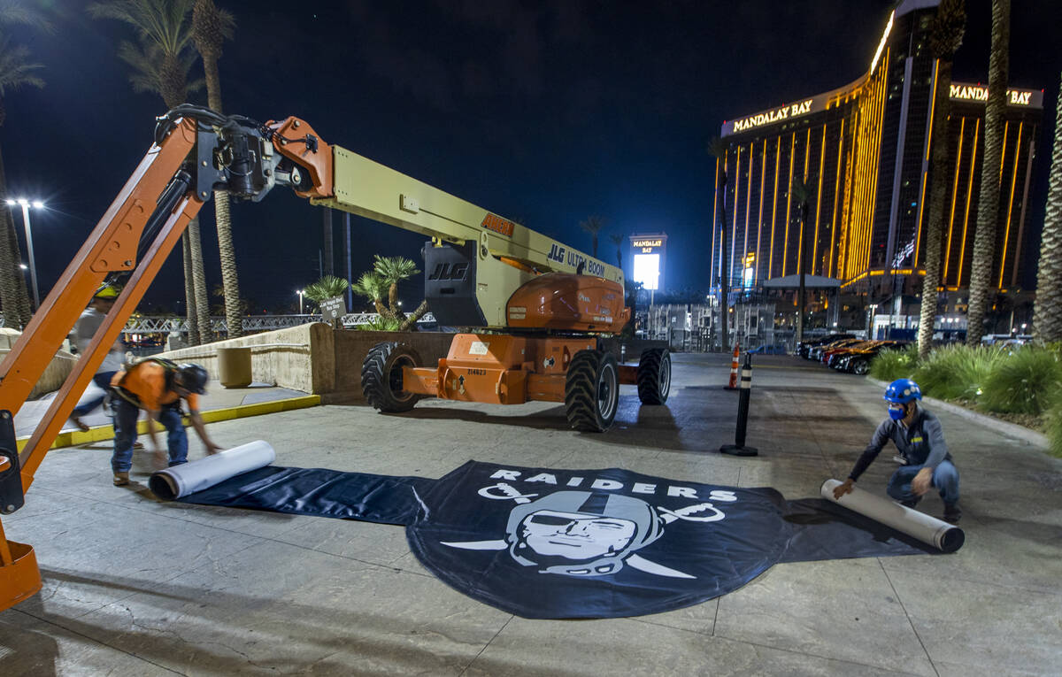 Billy Baker, left, and Miguel Lopez with Access Solutions unfurl a Raiders eye patch to be hung ...