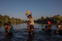 A little girl holds her stuffed animal high above the water as migrants, many from Haiti, wade ...
