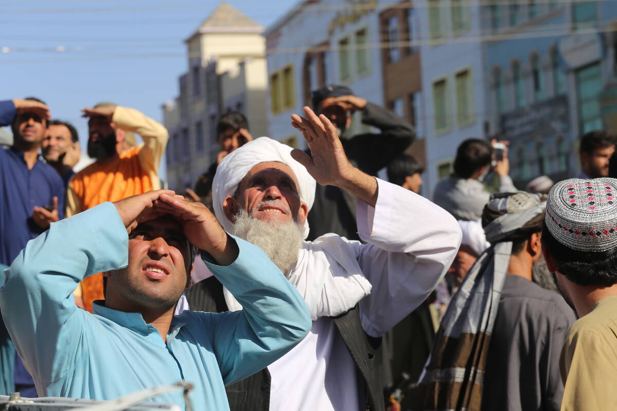 People look up at a dead body hanged by the Taliban from a crane in the main square of Herat ci ...