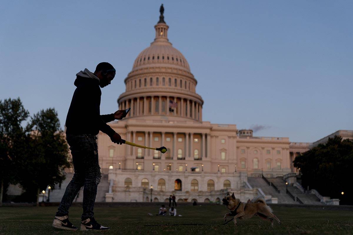 The U.S Capitol is visible at sunset as a man plays fetch with a dog in Washington, Thursday, S ...