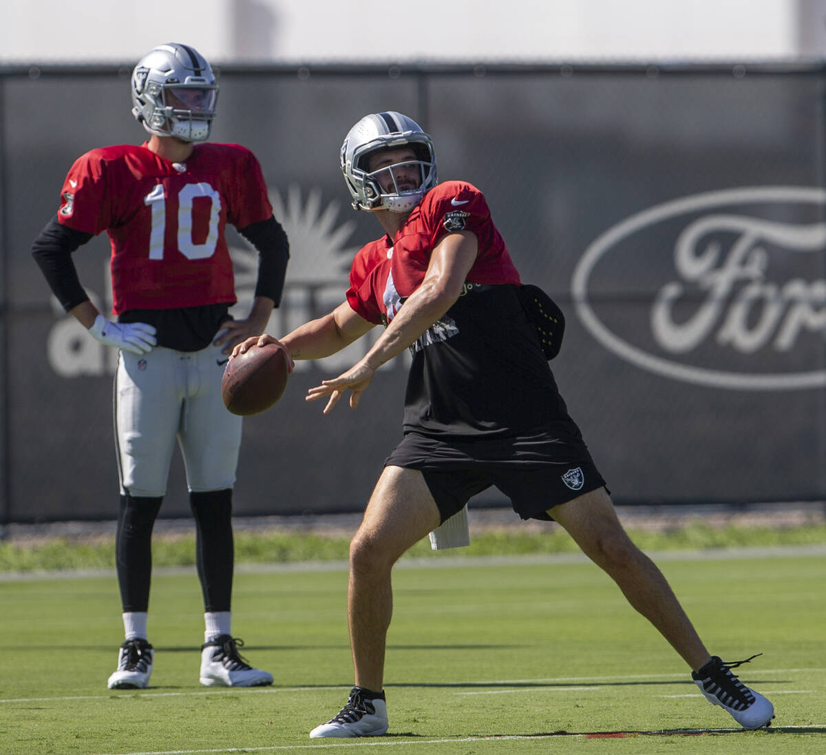 Raiders quarterback Kyle Sloter looks on as Raiders quarterback Derek Carr (4) prepares to thro ...