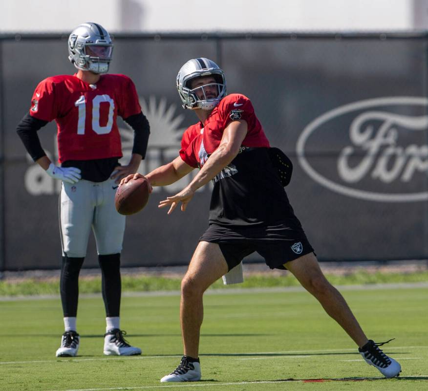 Raiders quarterback Kyle Sloter looks on as Raiders quarterback Derek Carr (4) prepares to thro ...