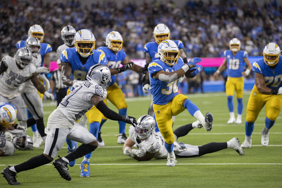 Los Angeles Chargers running back Austin Ekeler (30) bursts through the hole past Raiders corne ...