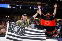 Raiders fans hold up a flag as a Chicago Bears fan cheers during an NFL game between the teams ...