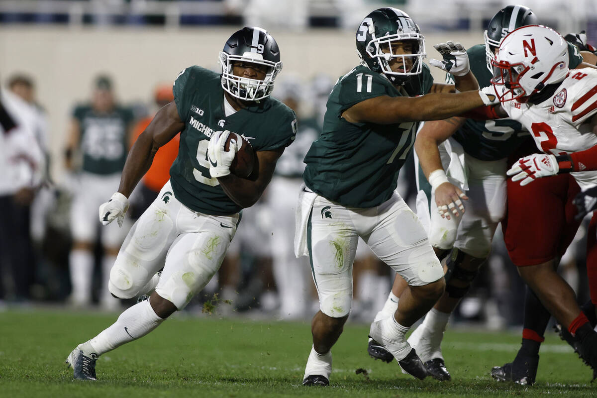 Michigan State's Kenneth Walker III, left, rushes against Nebraska's Caleb Tannor, right, as Mi ...